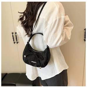 Détail du sac bandoulière en nylon noir avec nœud et logo en métal sur l'épaule d'un modèle
