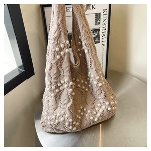 Detail of beige knit tote bag with white pearl wave patterns on a silver table