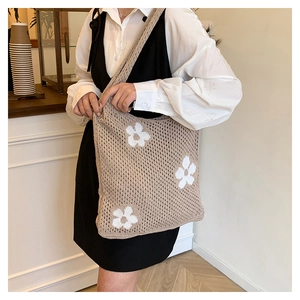 Close-up of beige knit shoulder bag with white floral pattern in a cozy cafe setting