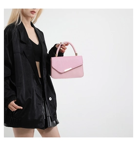 Detail view of pink leather underarm bag with asymmetric flap and metal trim on black suit