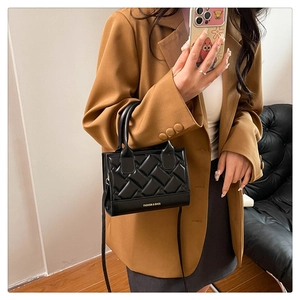 Close-up of black quilted small square bag with top handle worn on a brown blazer