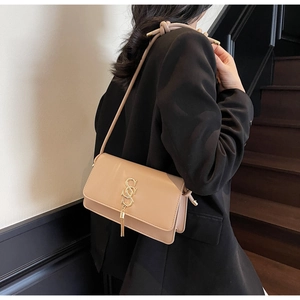 Detail of beige crossbody bag with gold letter hardware and metallic tassel pendant