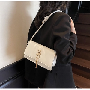 Detailed view of white patent leather bag with gold SS buckle and elegant tassel charm