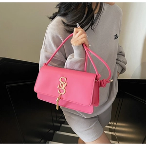 Detail of bright pink crossbody bag with gold SS logo and stylish tassel on dark background