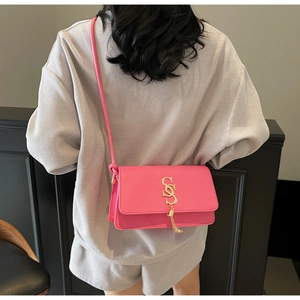 Detail of bright pink crossbody bag with gold letter logo and metal chain tassel