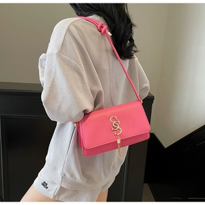 Detail of fuchsia leather square bag featuring a gold S letter and tassel on a model