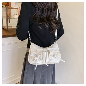 Detail of cream white bow shoulder bag with pockets and smooth leather texture on a model