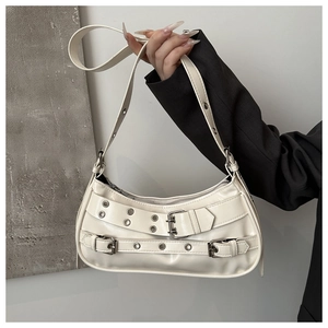 Detail of cream shoulder bag featuring silver metallic eyelets and adjustable buckle strap