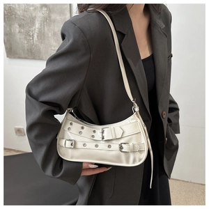 Detailed close-up of cream patent leather shoulder bag with silver rivet buckle straps