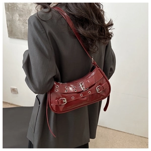 Macro detail of wine red glossy patent leather shoulder bag with punk metal eyelet straps