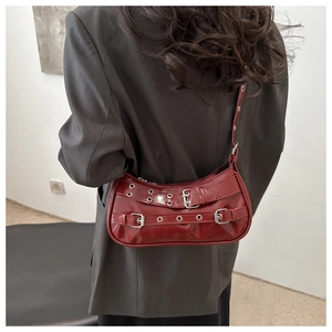 Detail of burgundy glossy shoulder bag featuring punk silver buckles and metal eyelets