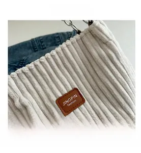 Macro shot of off-white corduroy tote texture with brown leather logo and metal chain detail