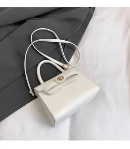Detail of white leather handbag featuring gold twist lock and adjustable shoulder strap