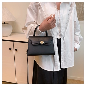 Close-up of black leather bag featuring a gold round lock buckle and curved lid detail