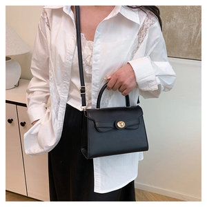 Detail of black crossbody bag with gold clasp and bow accent worn with white lace shirt