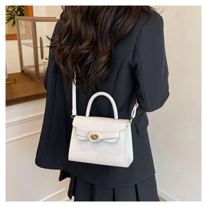 Detailed view of a white leather crossbody bag featuring a gold twist lock and top handle