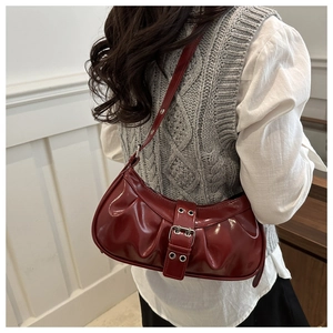 Detail showing dark red glossy patent leather shoulder bag with buckle strap on model