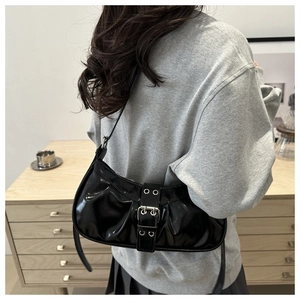 Detail of black patent leather hobo bag with adjustable metallic buckle on model shoulder