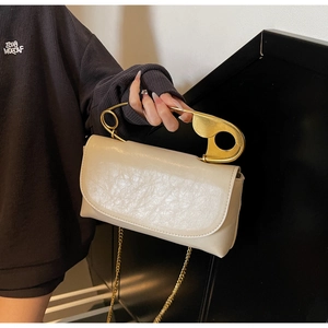 Dettaglio della borsa beige testurizzata con manico creativo a forma di spilla da balia dorata