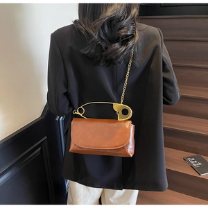 Détail du sac en similicuir caramel avec poignée en forme d'épingle de nourrice dorée et chaîne