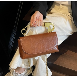 Dettaglio borsa in pelle marrone con manico a forma di spilla dorata e catenella