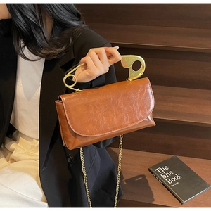 Dettaglio borsa in pelle marrone caramello con grande manico in metallo a forma di spilla
