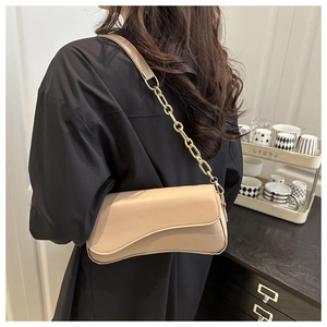 Beige wave-flap shoulder bag with gold chain strap shown on a model for scale