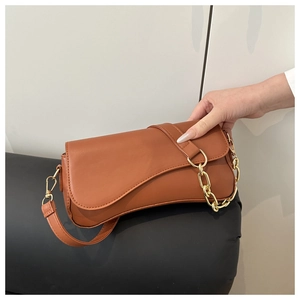 Detailed view of caramel brown saddle bag with asymmetrical flap and gold chain strap