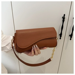 Detail of caramel leather handbag featuring gold chain handle and asymmetric saddle flap