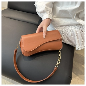 Detail of caramel leather crossbody bag with asymmetric flap and golden chain strap