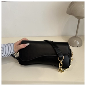 Detail of minimalist black matte leather crossbody bag with chunky gold chain decoration