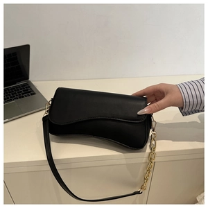 Detail of black leather crossbody bag with chunky gold chain on a minimalist desk