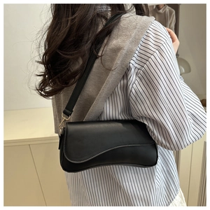 Close-up of black leather baguette bag with curved flap and gold metal hardware hooks