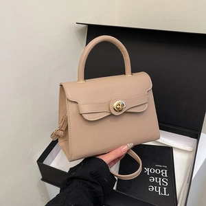 Beige leather Kelly style handbag with gold buckle closure and top handle shown in hand