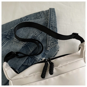 Detail of off-white nylon crossbody bag showing woven rope zipper pulls and black strap