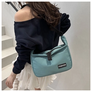Detail of teal nylon crossbody bag with fashion label and adjustable strap on a staircase