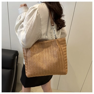 Detail of woven straw tote bag with brown leather and silver metal chain strap