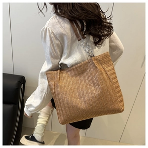 Detailed texture of woven straw tote bag with brown leather and chain shoulder strap