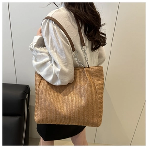 Detail of woven straw tote bag featuring brown leather shoulder straps and silver chain link