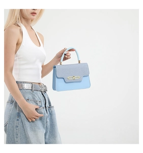Detail of light blue handbag featuring a textured flap and gold metal lock clasp