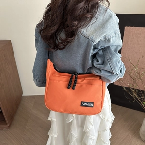 Bright orange nylon crossbody bag with fashion label shown on a model in a casual outfit