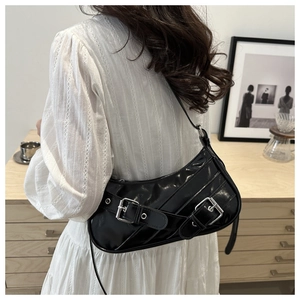 Detail of black patent leather baguette bag with silver buckles worn over the shoulder