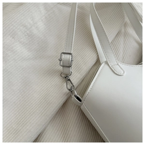 Close-up of silver metal hardware and adjustable strap on a white leather bucket bag