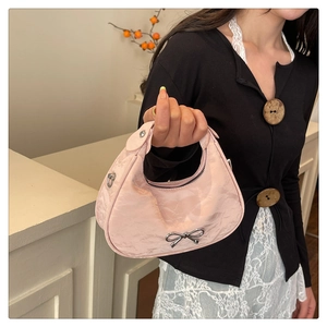 Detail of light pink crescent handbag featuring pleated texture and metal bow fastener