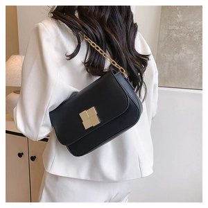 Detail of a black leather handbag with a chunky gold chain strap worn by a model