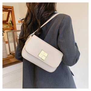 Model wearing a minimalist cream shoulder bag with a square gold clasp in a cafe setting