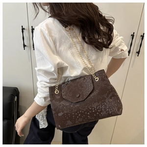 Close-up of brown snakeskin pattern shoulder bag with golden chain strap on a model