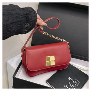 Close-up of red shoulder bag featuring a gold square buckle and leather chain strap