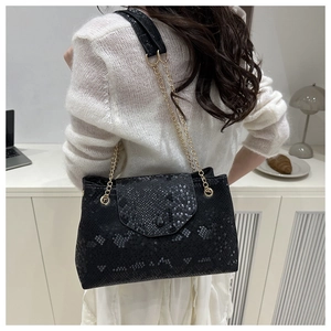 Detail of black faux snake texture tote bag with gold chain strap on a desk