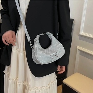 Silver metallic crescent bag with bow detail worn by a model in a black blazer